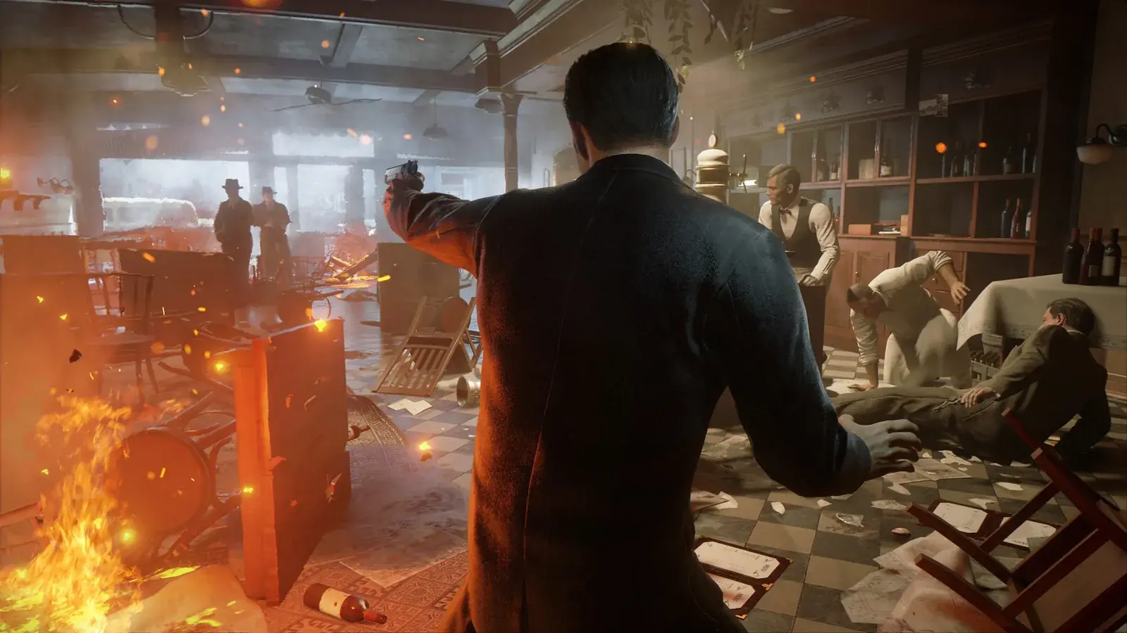 Tommy míří pistolí v rozstříleném baru, převrácené stoly a oheň, Mafia: Definitive Edition