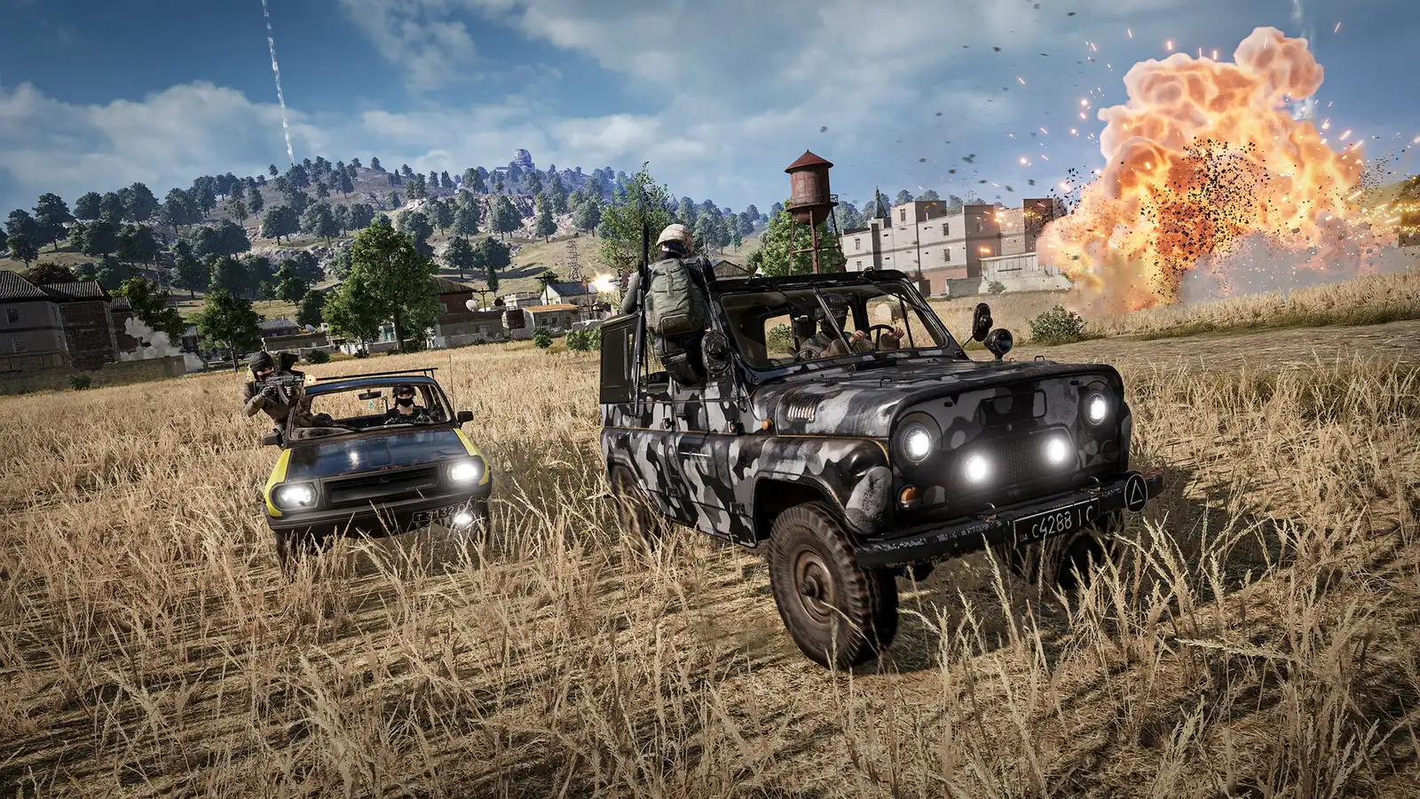 Squad ve dvou autech projíždí polem k vesnici, vpravo vybuchuje nálož